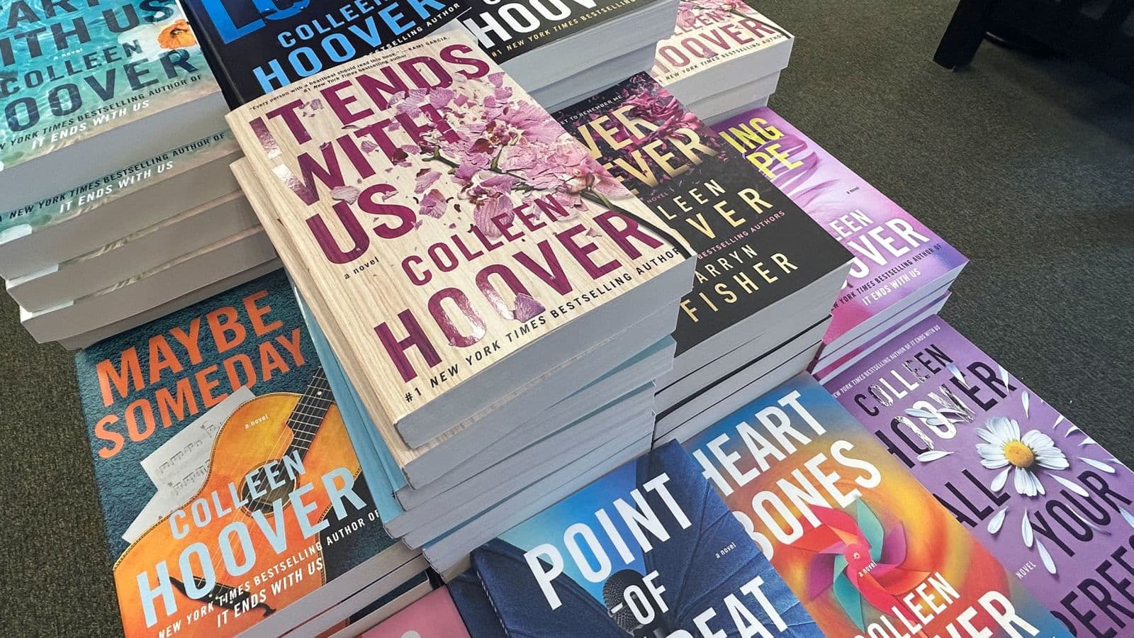 Colleen Hoover speaking onstage against a pink and purple backdrop